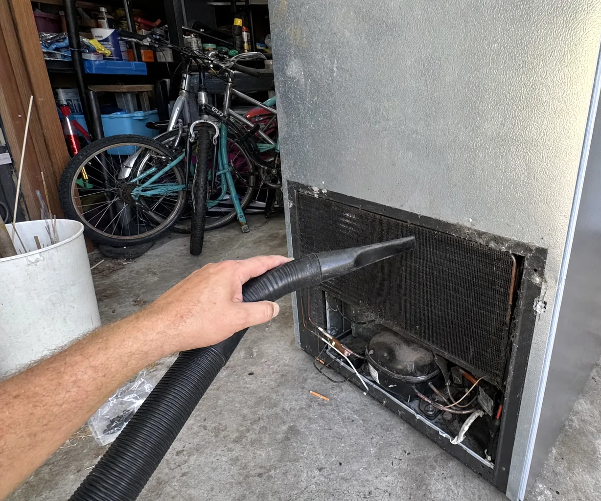 Left crop of the condenser cleaning: dusty aluminium fins, the vacuum nozzle against them and the open grille aperture.